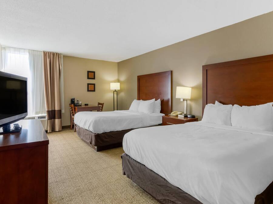 A hotel room with two beds, a desk, a television, and a lamp.