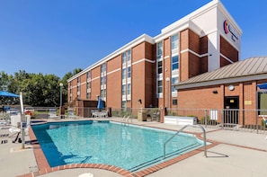 A hotel with a swimming pool, outdoor seating, and a brick facade.