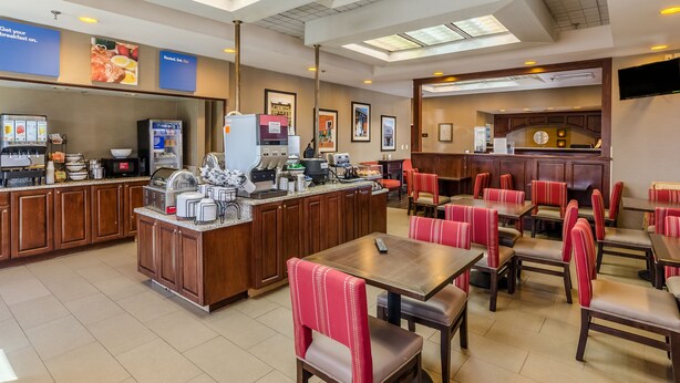 A hotel breakfast area with a self-service counter, seating, and a TV screen. - Comfort Inn Blacksburg University Area (Christiansburg)
