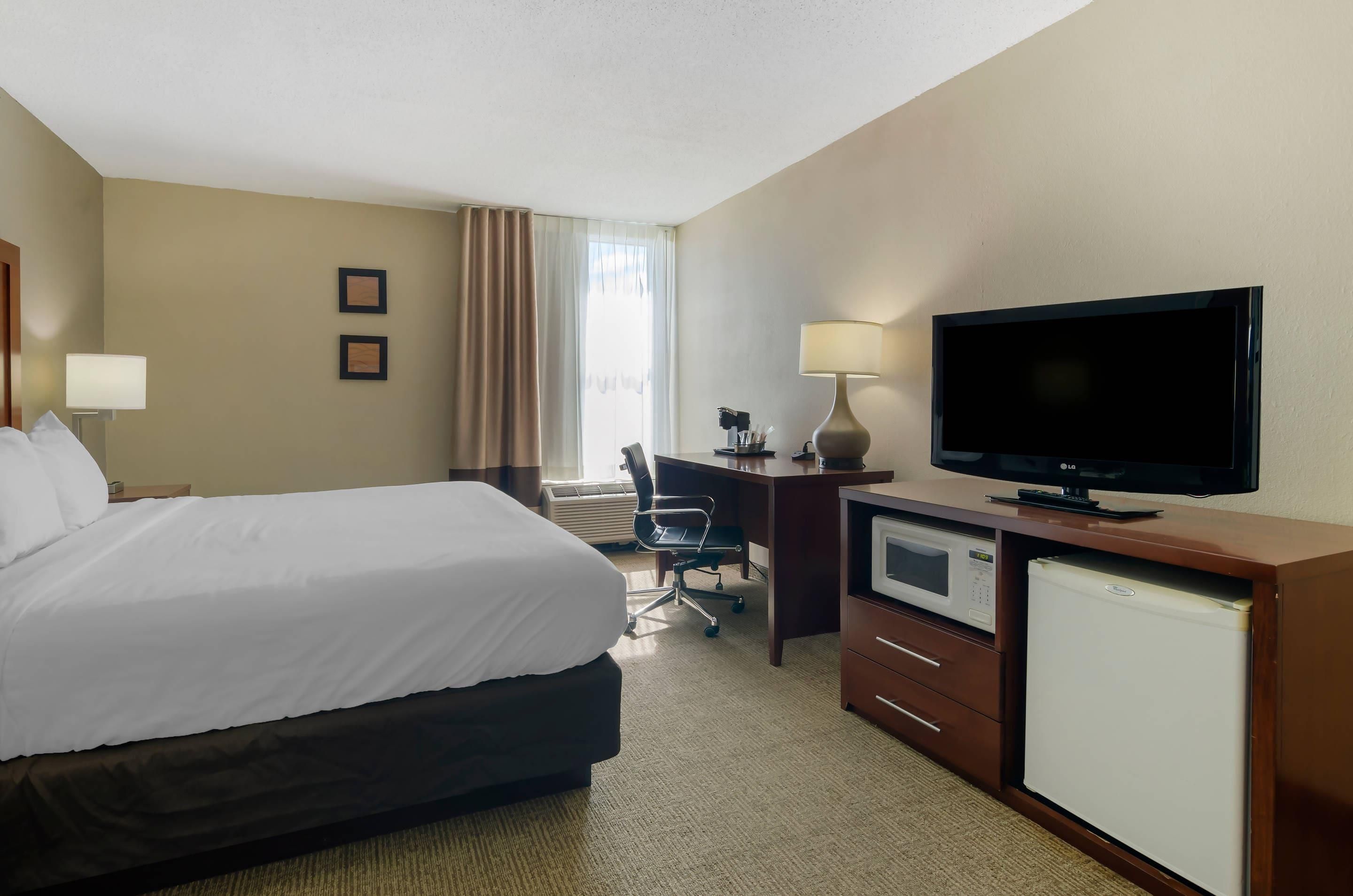 A hotel room with a bed, desk, television, and a mini-fridge.