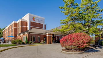 A Comfort Inn hotel with a brick facade, a covered entrance, and a landscaped area with a red flowering bush.