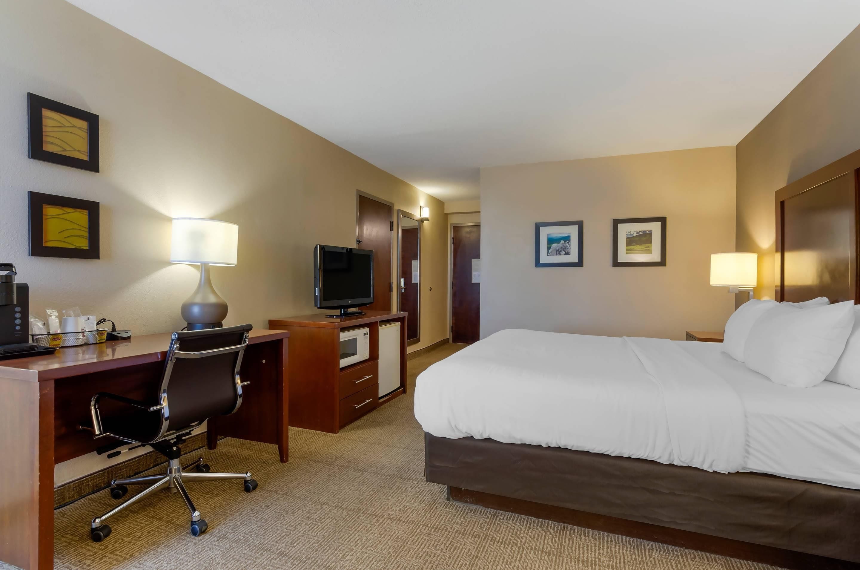Ein Hotelzimmer mit Bett, Schreibtisch, Stuhl, Fernseher und zwei gerahmten Bildern an der Wand.