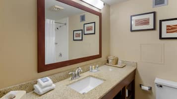 A bathroom with a sink, mirror, towel dispenser, toilet, and framed artwork on the wall.