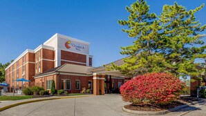A Comfort Inn hotel with a brick facade, a covered entrance, and a well-maintained front lawn with a red flowering bush. - Comfort Inn Blacksburg University Area (Christiansburg)