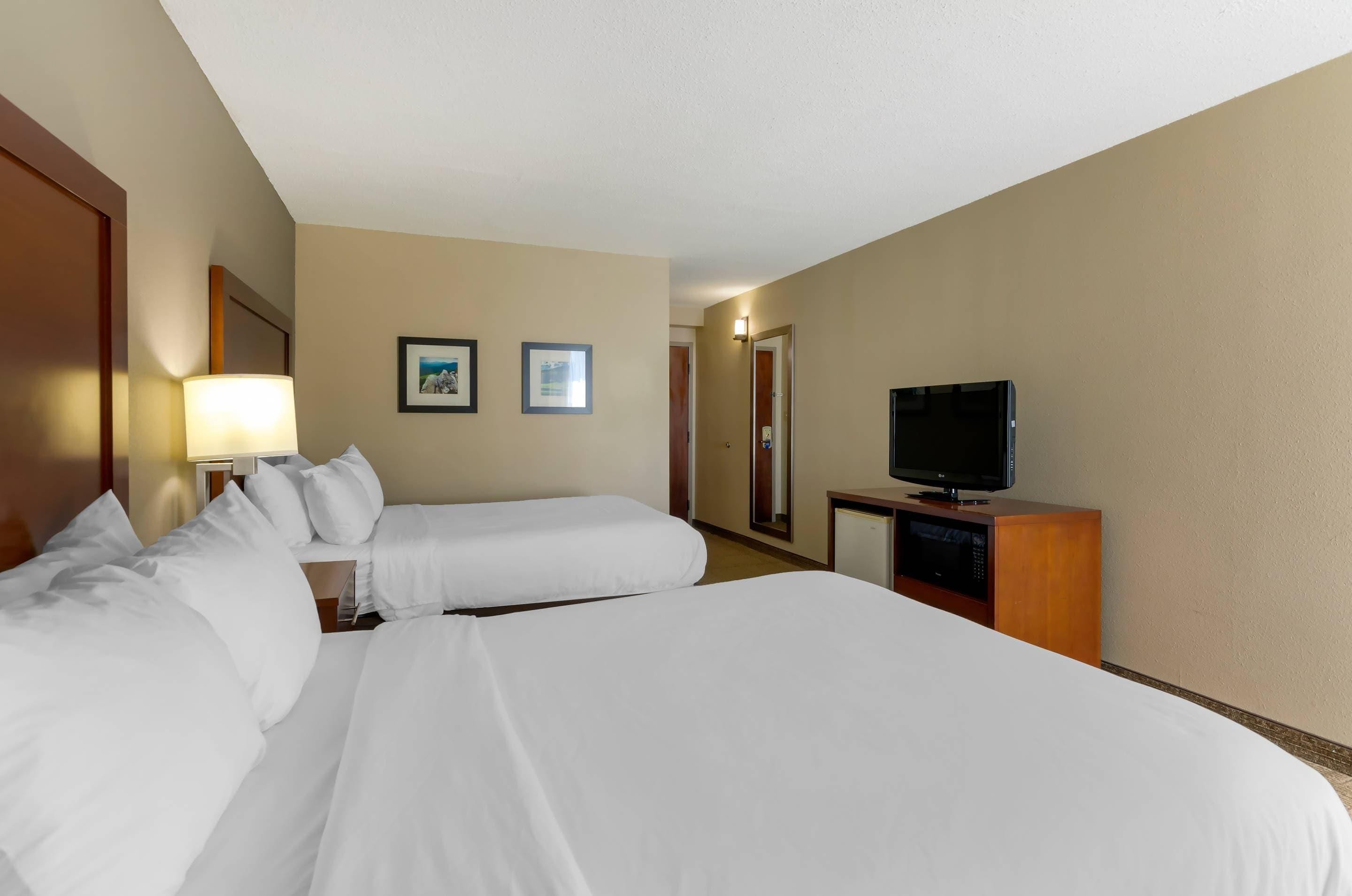 A hotel room with two beds, a television, a desk with a lamp, and two framed pictures on the wall.