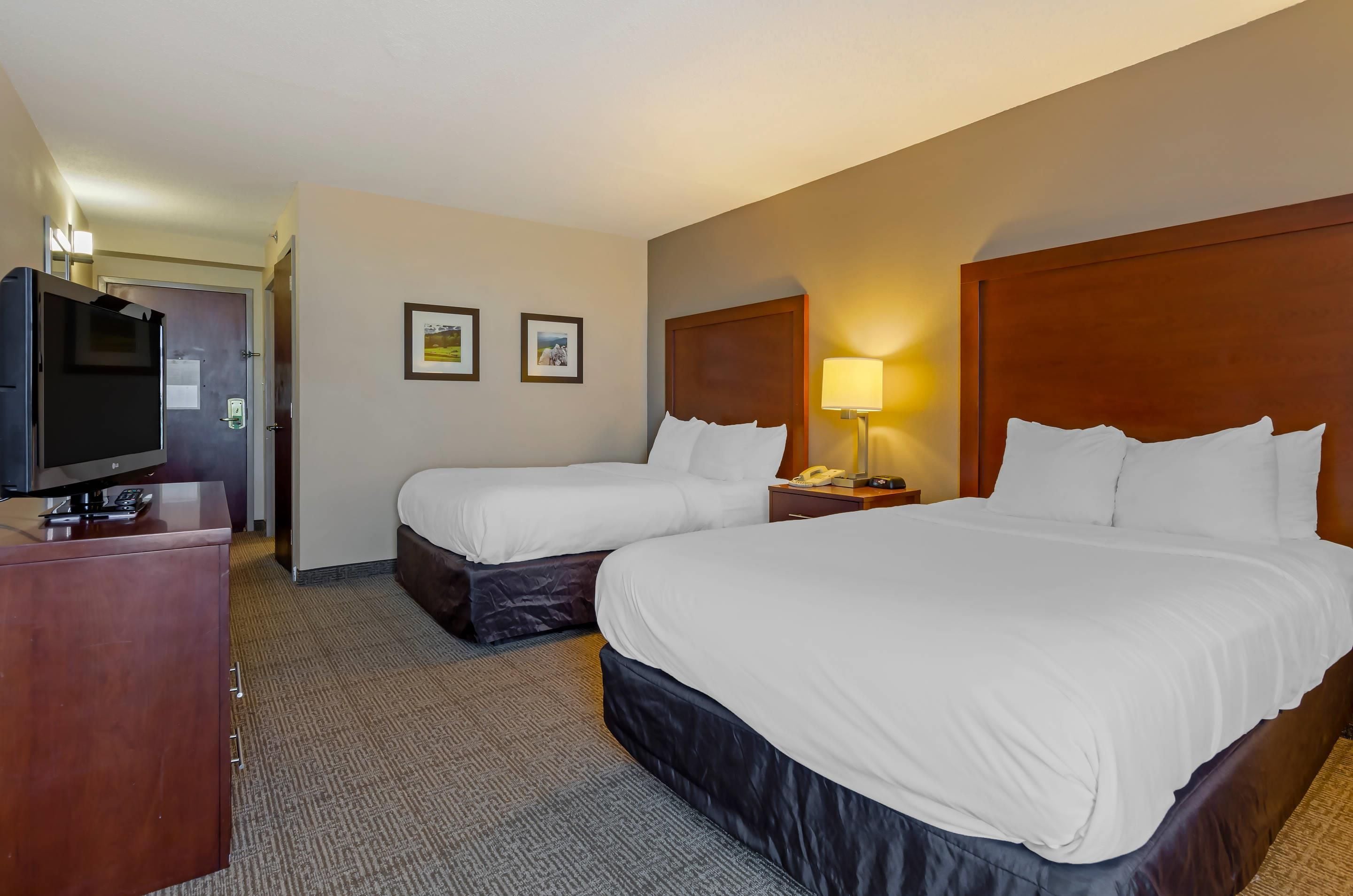A hotel room with two beds, a television, a desk, and a lamp.