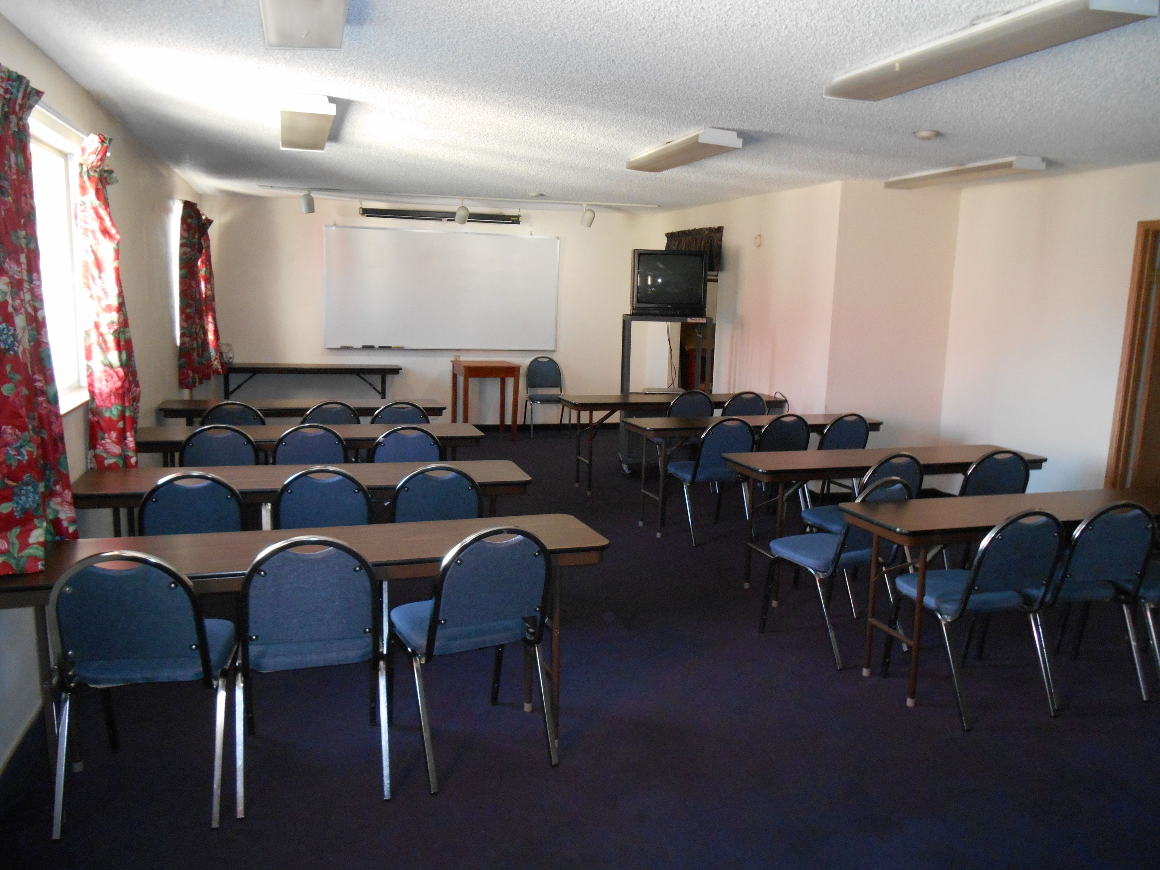 Ein Konferenzraum mit Tischen, Stühlen, einer Tafel und einem Fernseher.