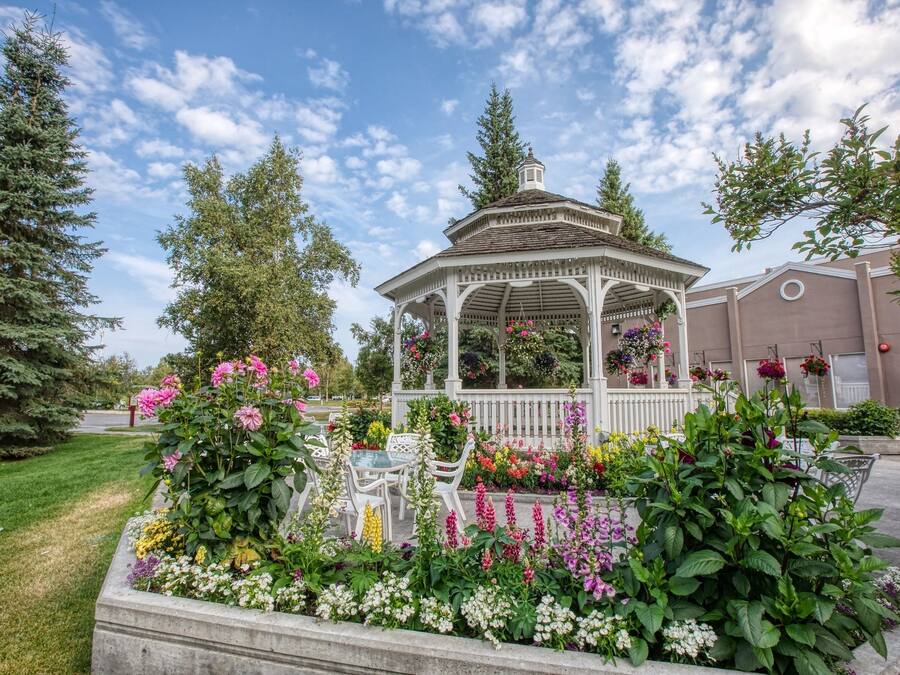 A gazebo surrounded by a flower garden with a clear sky.