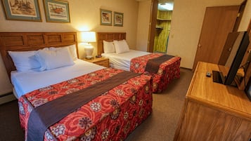 Habitación de hotel con dos camas, cabecero de madera, escritorio con espejo y televisor.