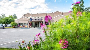 A building with a sign reading "Wedgewood Market Desk - Convention Center" with a parking lot and lush greenery in the foreground. - Wedgewood Resort (Fairbanks)