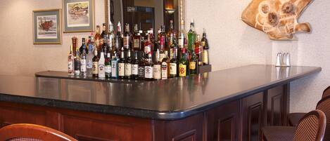 A bar area with a polished granite countertop, multiple liquor bottles, framed artwork, and a large mirror.