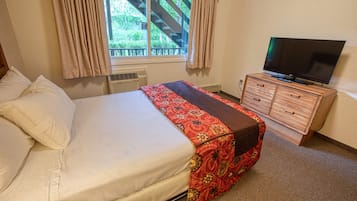 Een slaapkamer met een bed, een televisie op een dressoir en een raam met gordijnen.