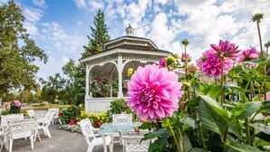 A gazebo with a glass table and white chairs, surrounded by lush greenery and vibrant flowers. - Wedgewood Resort (Fairbanks)