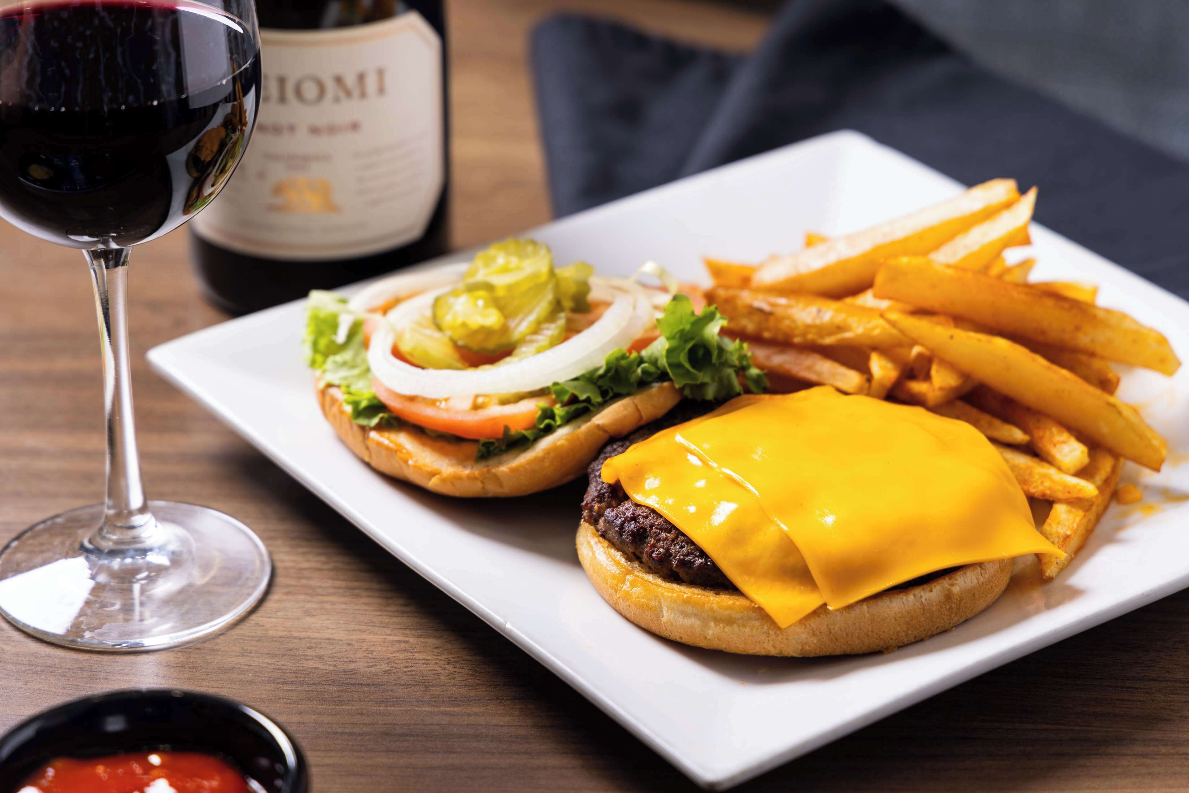 A plate with two burgers, fries, and a glass of red wine.