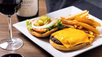 A plate with two burgers, fries, and a glass of red wine.