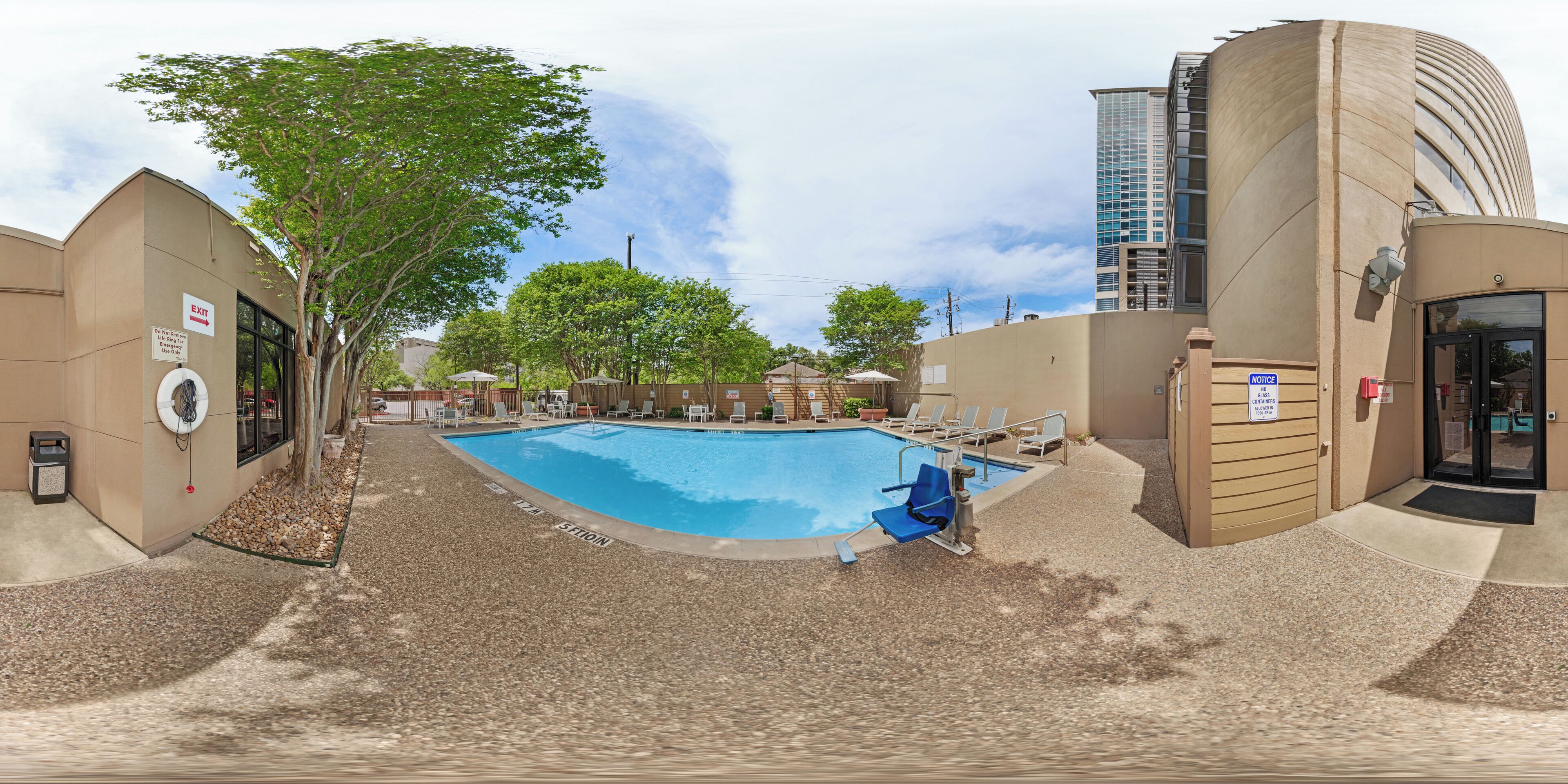 A swimming pool with lounge chairs, a tree, and a building with a curved facade.