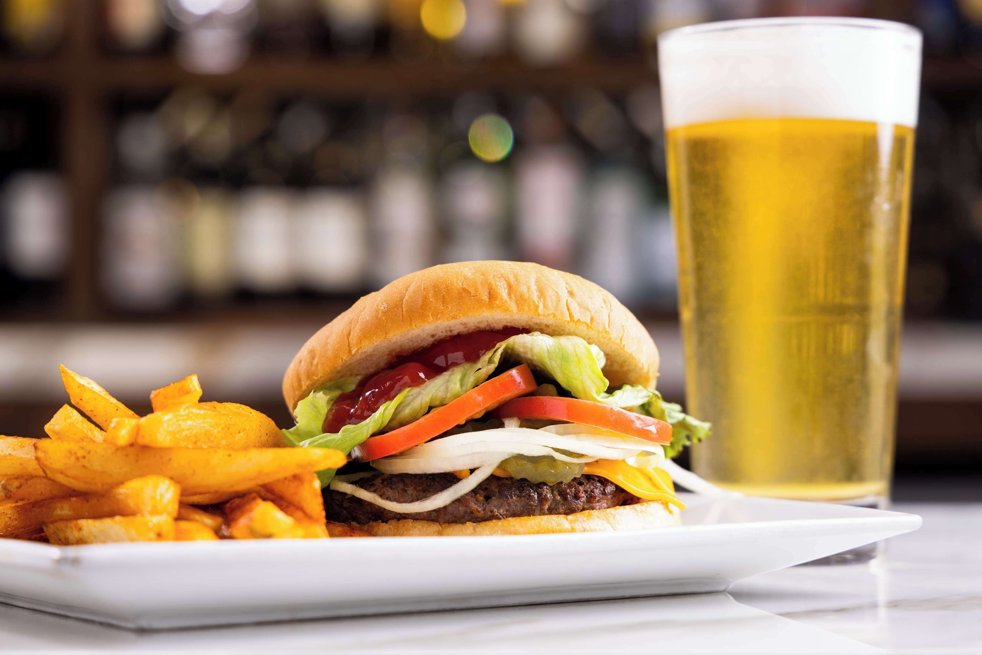 A burger with fries and a glass of beer on a white plate.