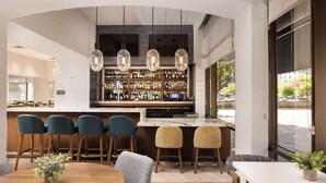 A modern bar area with a wooden bar counter, multiple hanging pendant lights, and a variety of bottles. There are bar stools and a seating area with a table and chairs. - DoubleTree by Hilton Houston Medical Center Hotel & Suites (Houston)