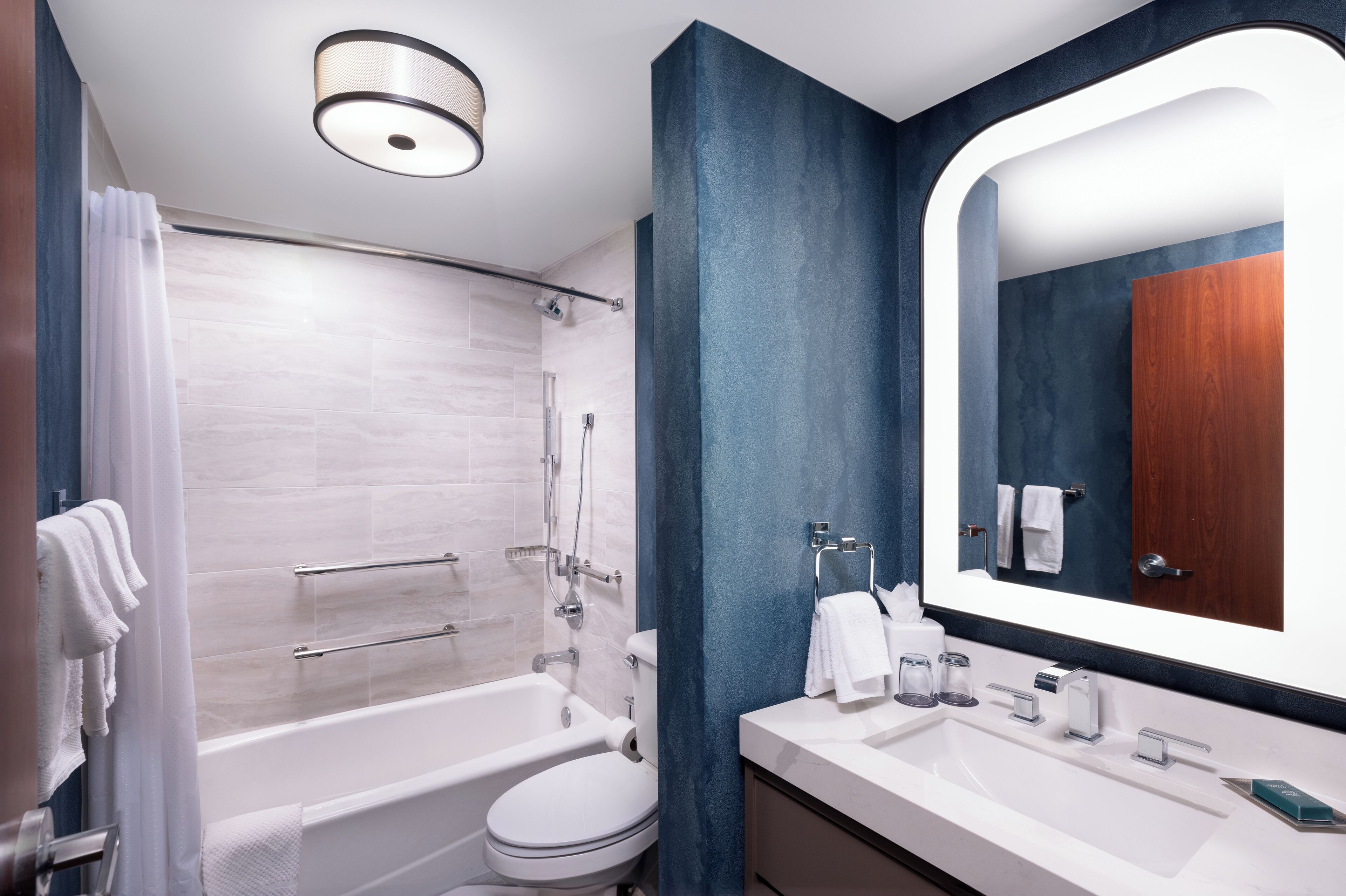 Un baño moderno con bañera, inodoro y lavabo, que incluye un espejo grande y una zona de ducha.