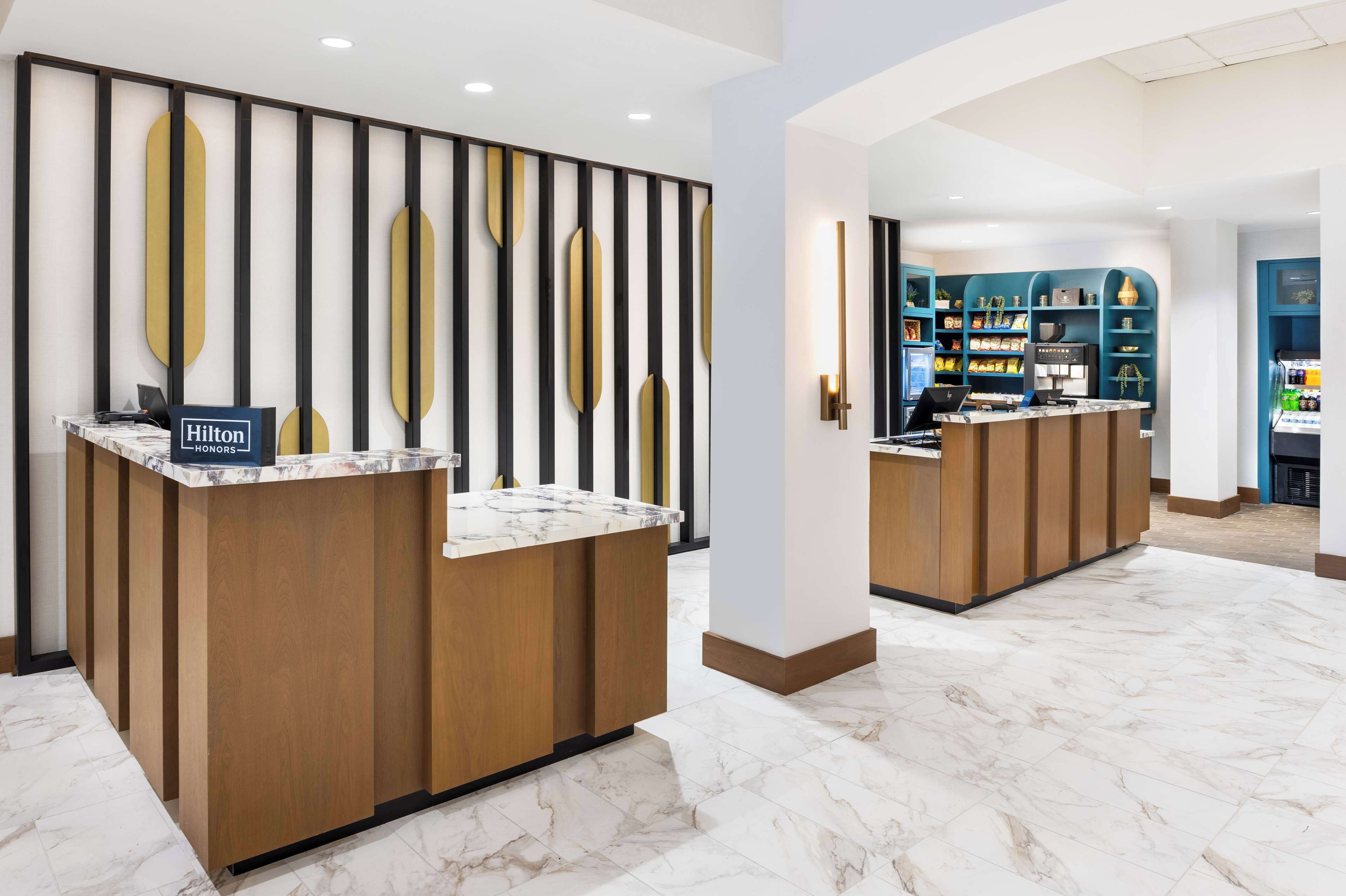 Ein Hotel-Empfangsbereich mit zwei Empfangstresen, Marmorboden und modernem Design mit vertikalen schwarzen und goldenen Akzenten.
