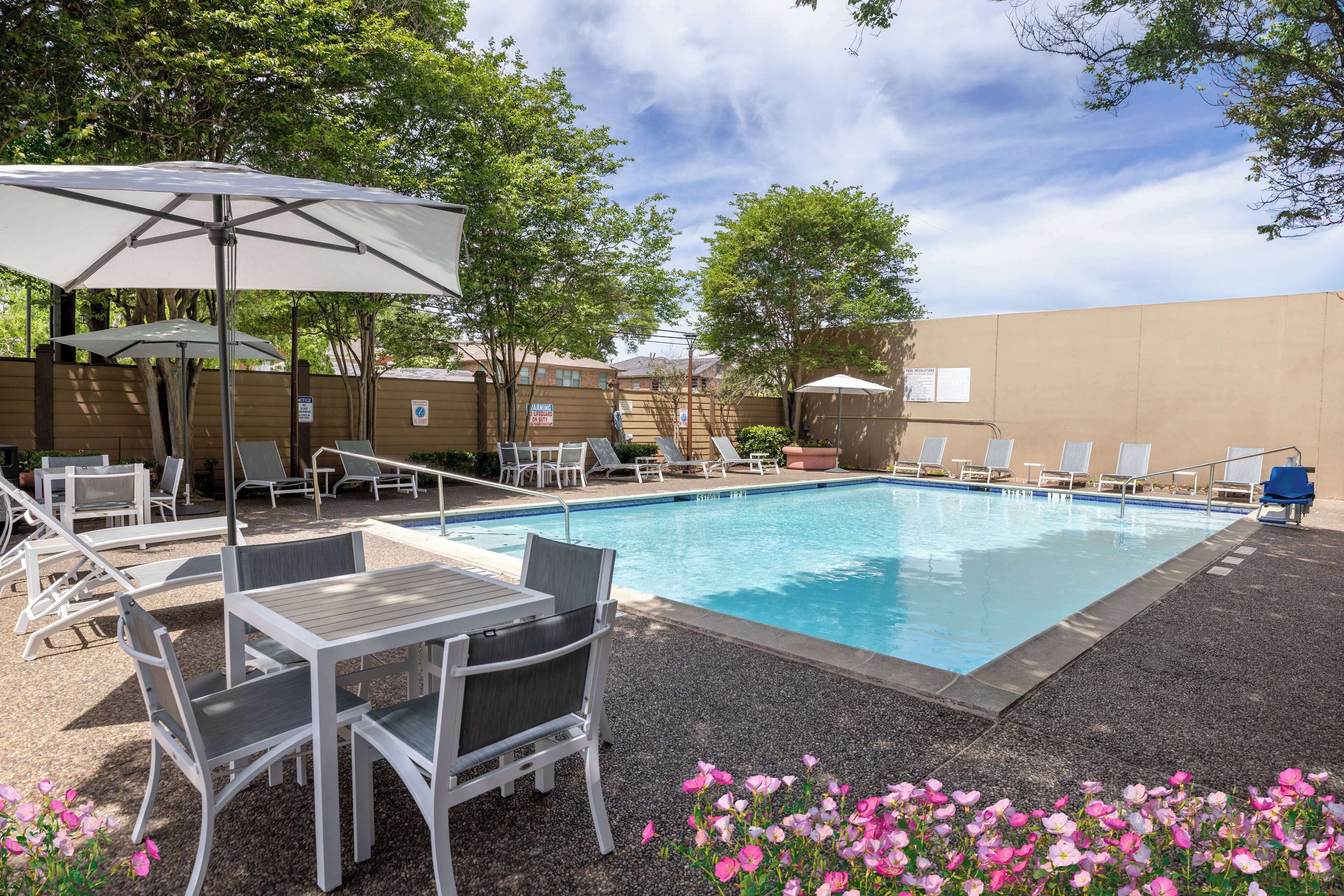A swimming pool with lounge chairs and tables, surrounded by a fence and trees.