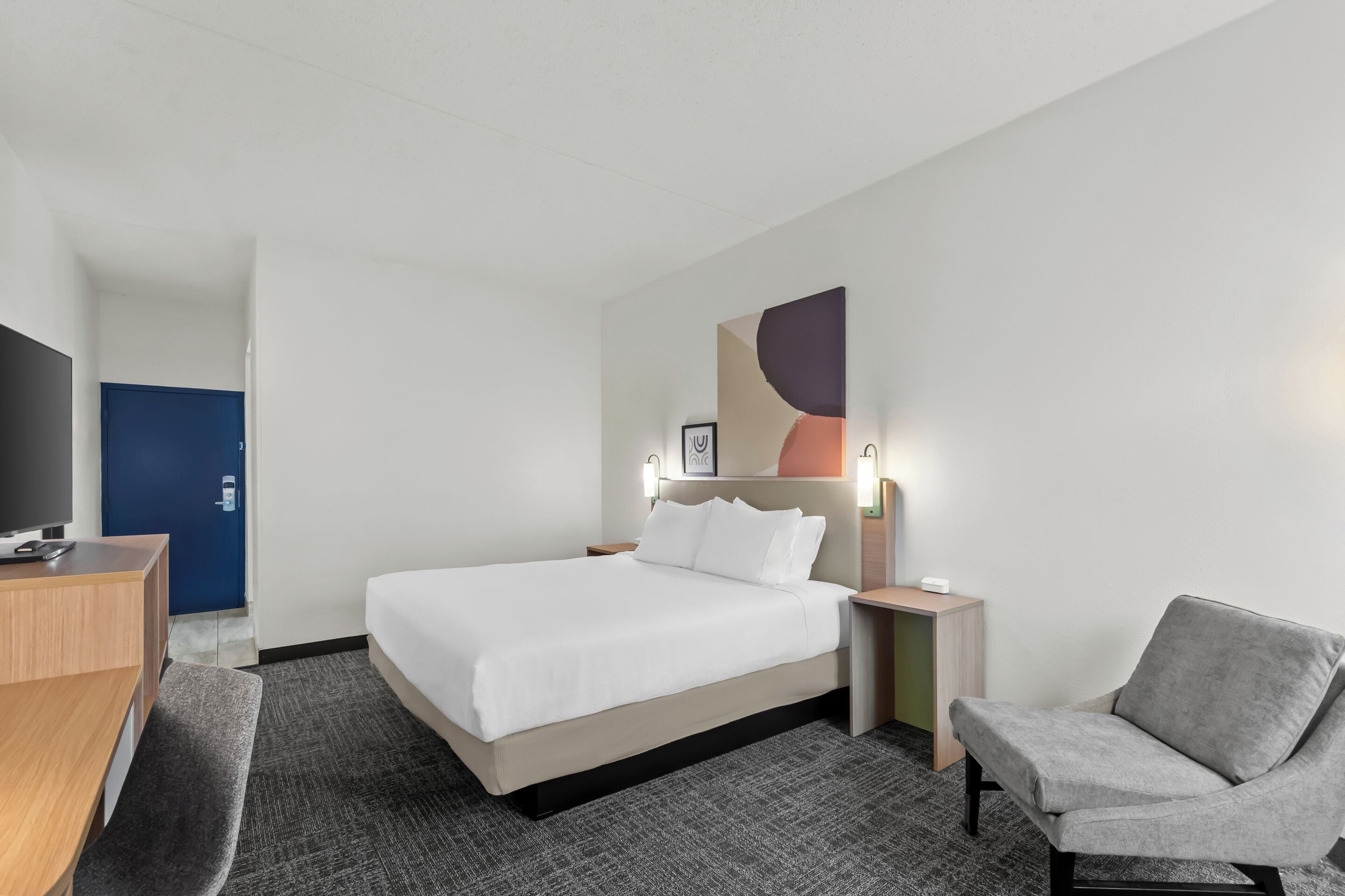 Habitación de hotel con cama, mesitas de noche, escritorio, silla y televisor.