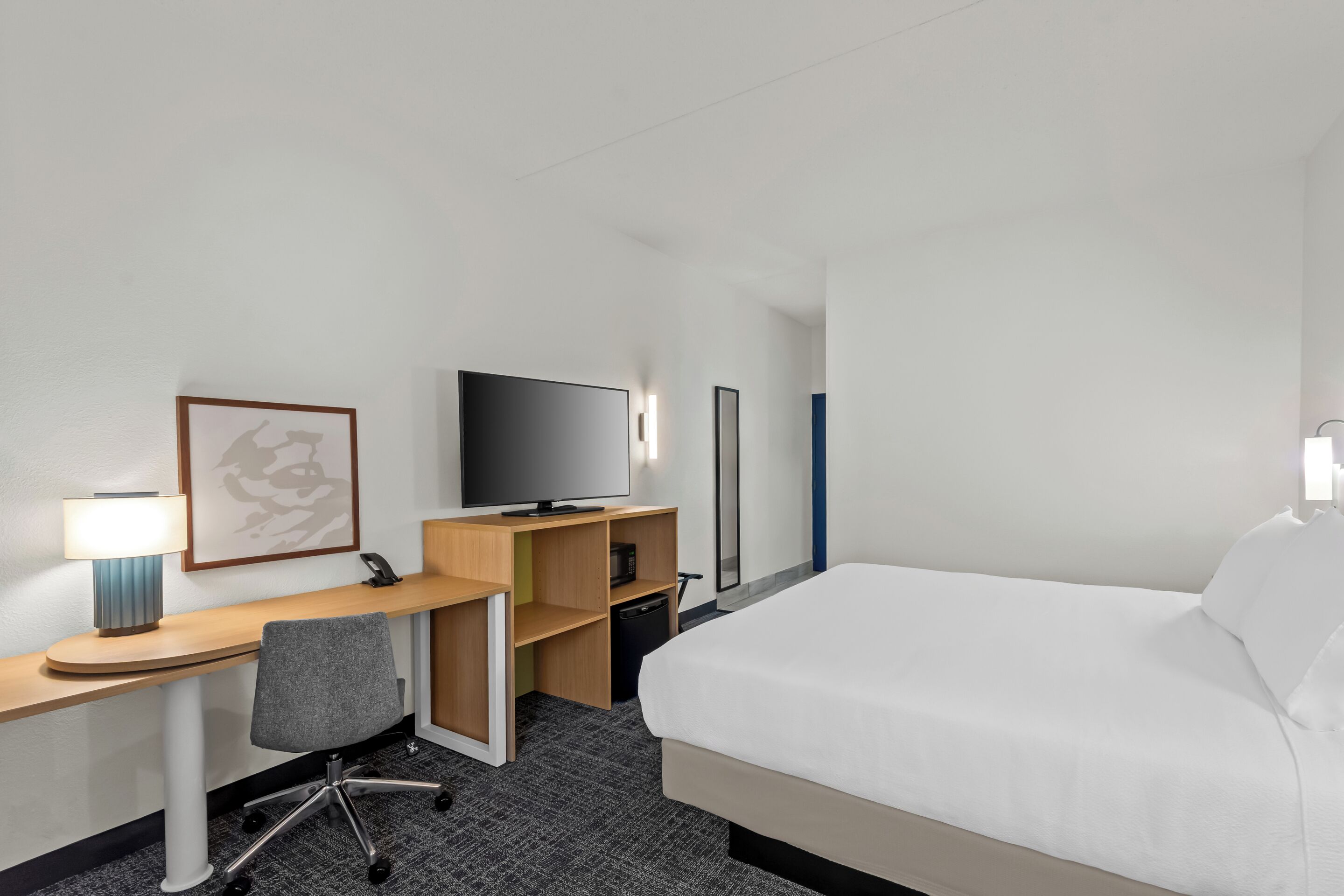 Une chambre d’hôtel avec un lit, un bureau et une chaise, une télévision et un tableau encadré au mur.