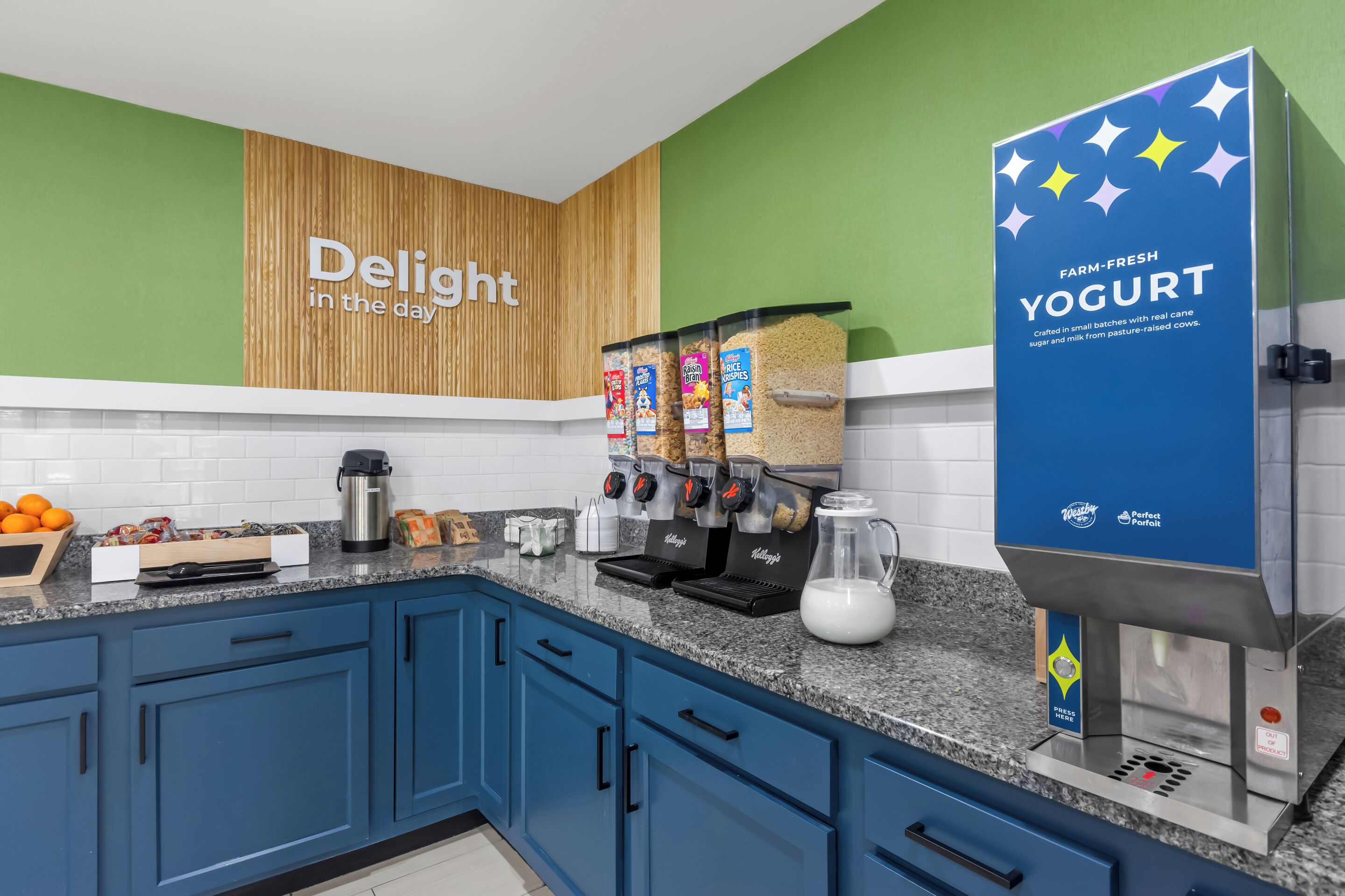 A modern kitchen with blue cabinets, a coffee machine, a yogurt dispenser, and a sign that reads "Delight in the day".