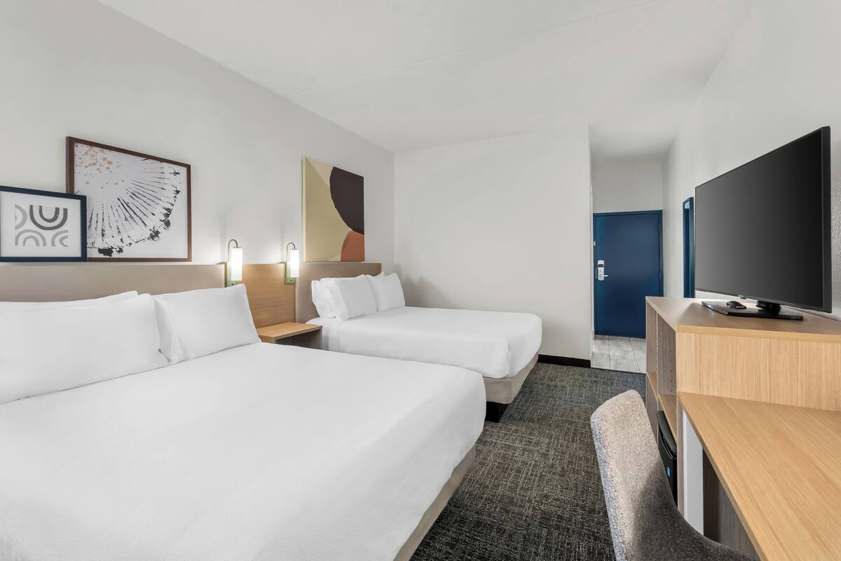 Ein Hotelzimmer mit zwei Einzelbetten, einem Schreibtisch, einem Flachbildfernseher und Bildern an den Wänden.