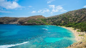 A coastal landscape with a beach, clear turquoise waters, and hills in the background. - Wayfinder Waikiki (Honolulu)