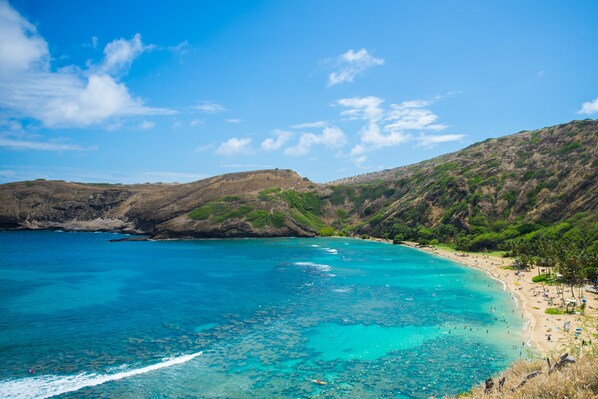 Paisaje costero con una playa, aguas turquesas cristalinas y colinas al fondo.