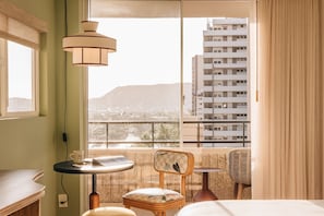 Habitación de hotel con balcón, vistas de la ciudad, una mesita redonda, una silla y una cama.