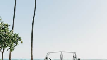 En vit servicebil parkerad på en väg med palmer och en strand i bakgrunden.