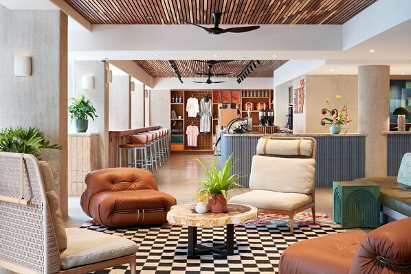 A spacious lobby with leather seating, a central wooden table with a plant, and a checkered floor. - Wayfinder Waikiki (Honolulu)