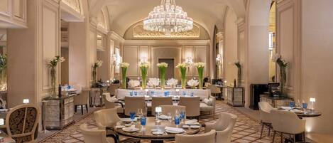 A spacious, elegantly decorated dining area with high ceilings, chandeliers, and floral arrangements.
