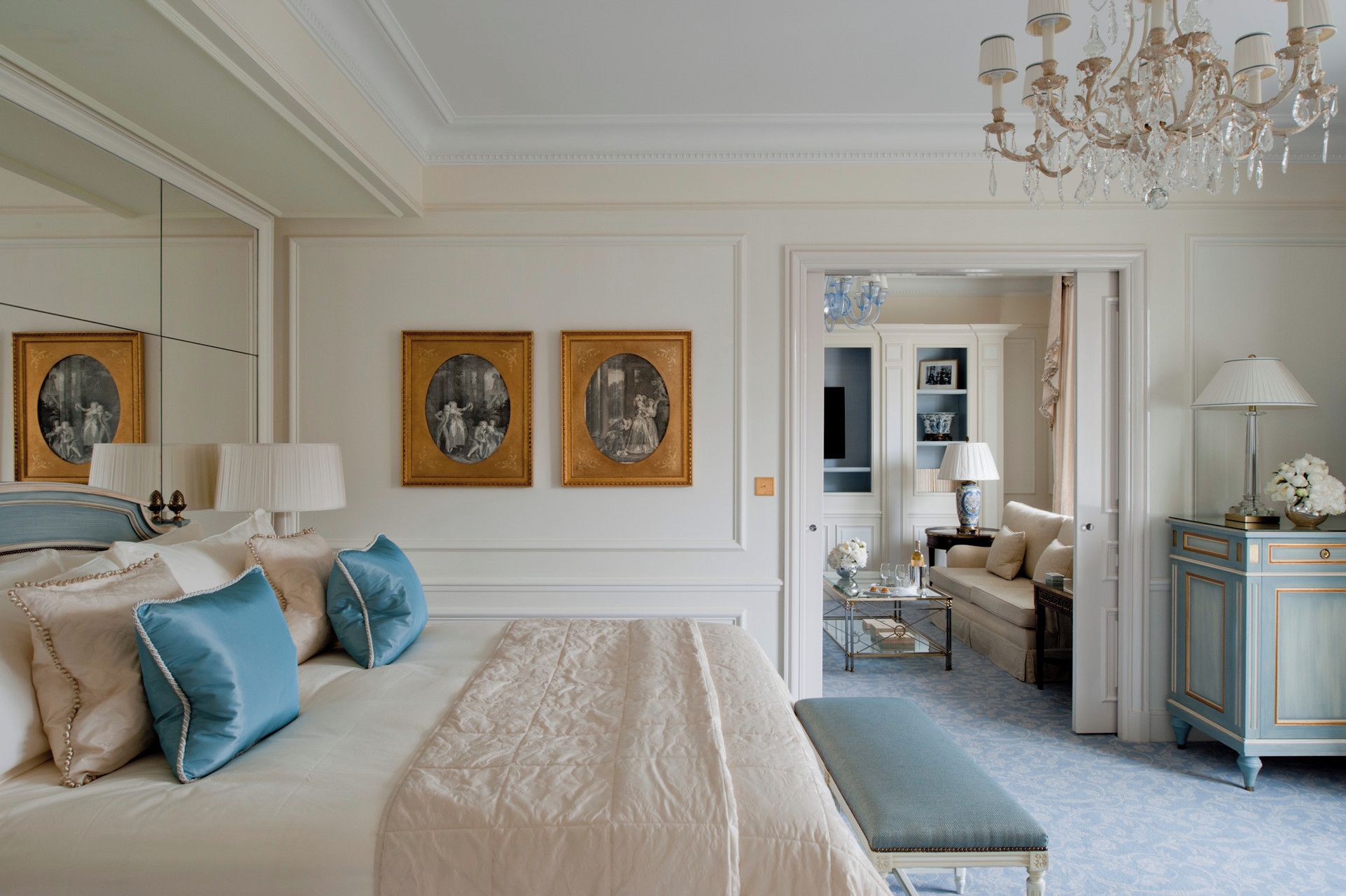 Una habitación de hotel con una cama grande, un área de descanso, una araña de cristal y obras de arte en las paredes.