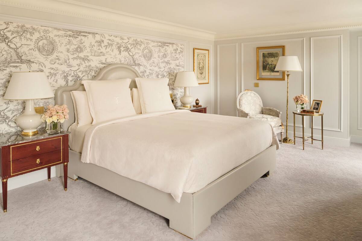 Une chambre à coucher classique avec un grand lit, deux tables de chevet avec des lampes, une chaise et une petite table avec une lampe.