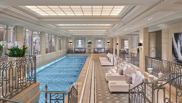 A luxurious indoor swimming pool with a tiled floor, surrounded by elegant seating and a glass railing.
