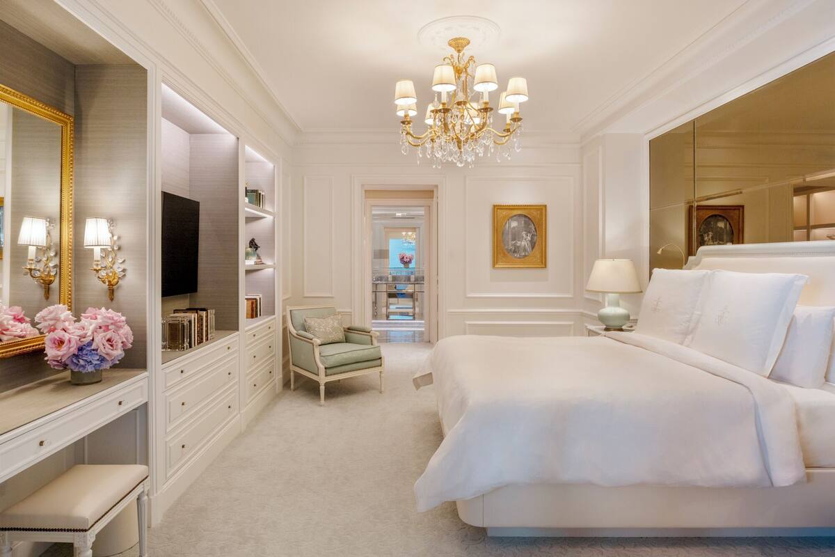 Une chambre à coucher luxueuse, dotée d’un grand lit, d’une coiffeuse avec un miroir et d’un lustre.