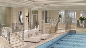 Una piscina interior lujosa con escalones de mármol y zonas de estar blancas.