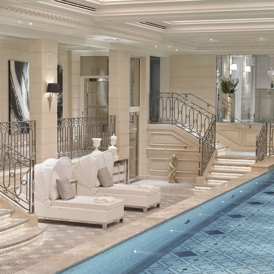 A luxurious indoor swimming pool with marble steps and white seating areas.