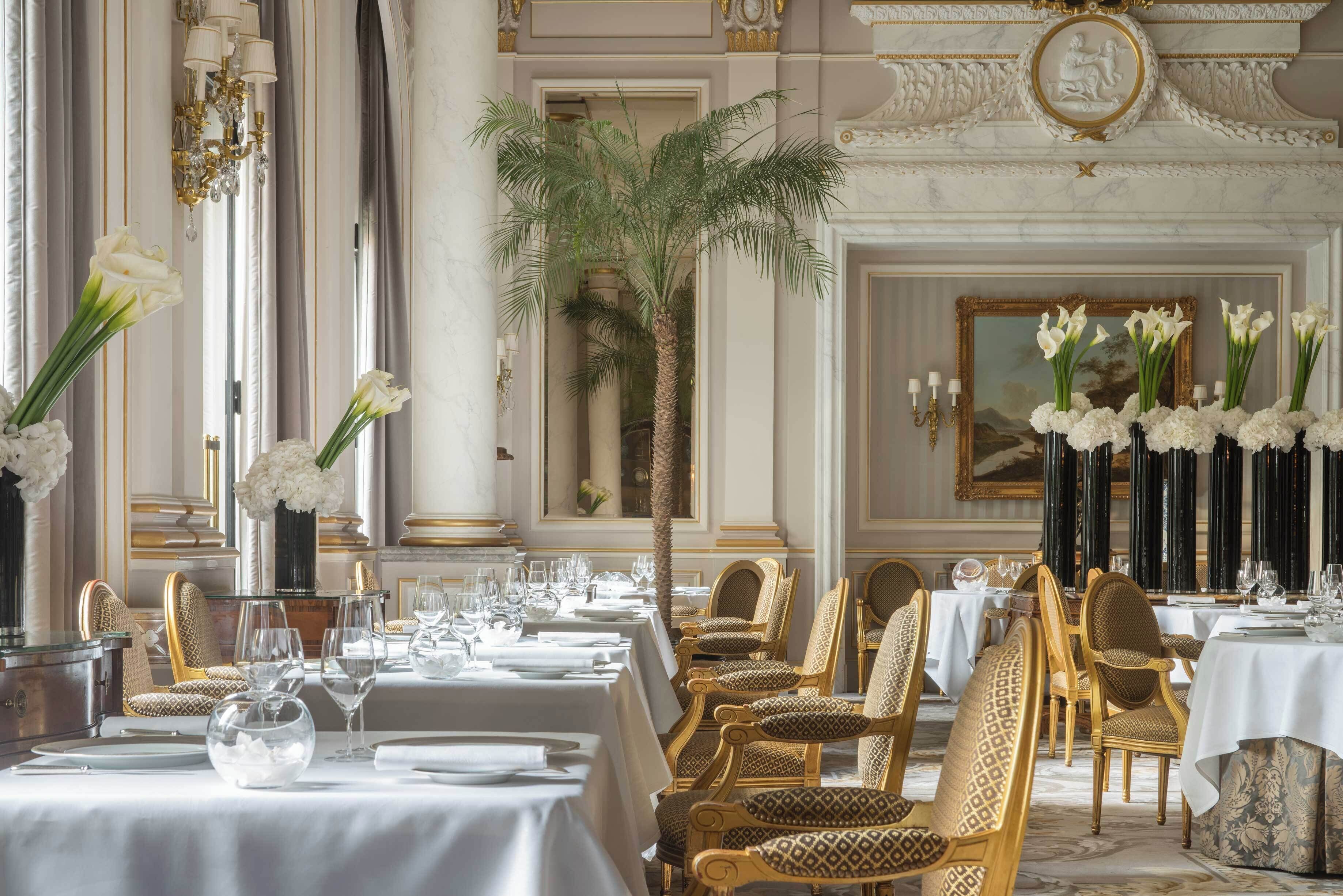 A formal dining room with long tables, gold chairs, and white floral arrangements.