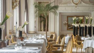 A formal dining room with long tables, gold chairs, and white floral arrangements.
