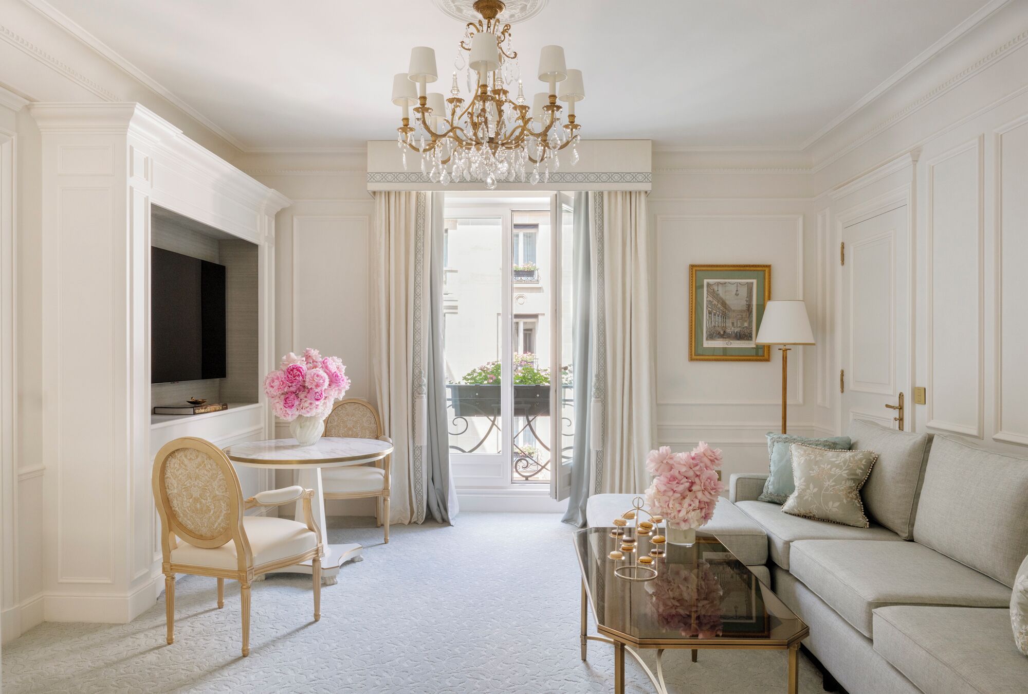 Un salon élégant et bien éclairé, agrémenté d’un lustre, d’un canapé, d’une table basse et d’un téléviseur.