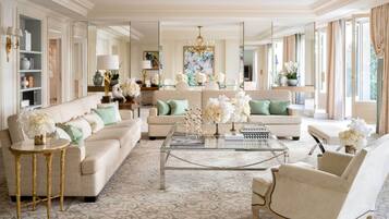 A spacious living room with a large sofa, a coffee table, and a chandelier. There are multiple seating options and a large mirror.