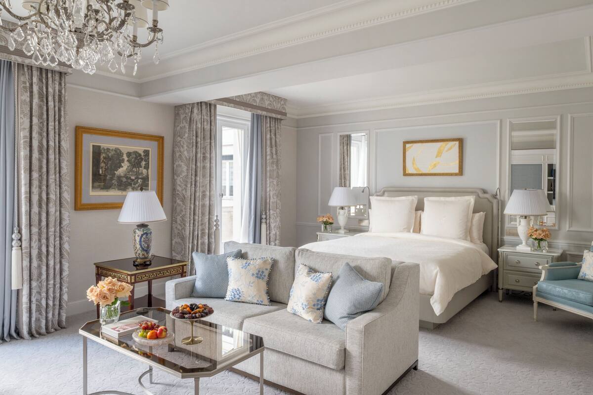 Une chambre spacieuse avec un grand lit, un canapé, une table basse en verre et un lustre.