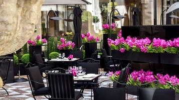 An outdoor café with tables and chairs, surrounded by potted plants and flowers.
