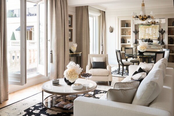 A spacious living room with a large window, a round coffee table, a sofa, and a dining area with a chandelier.