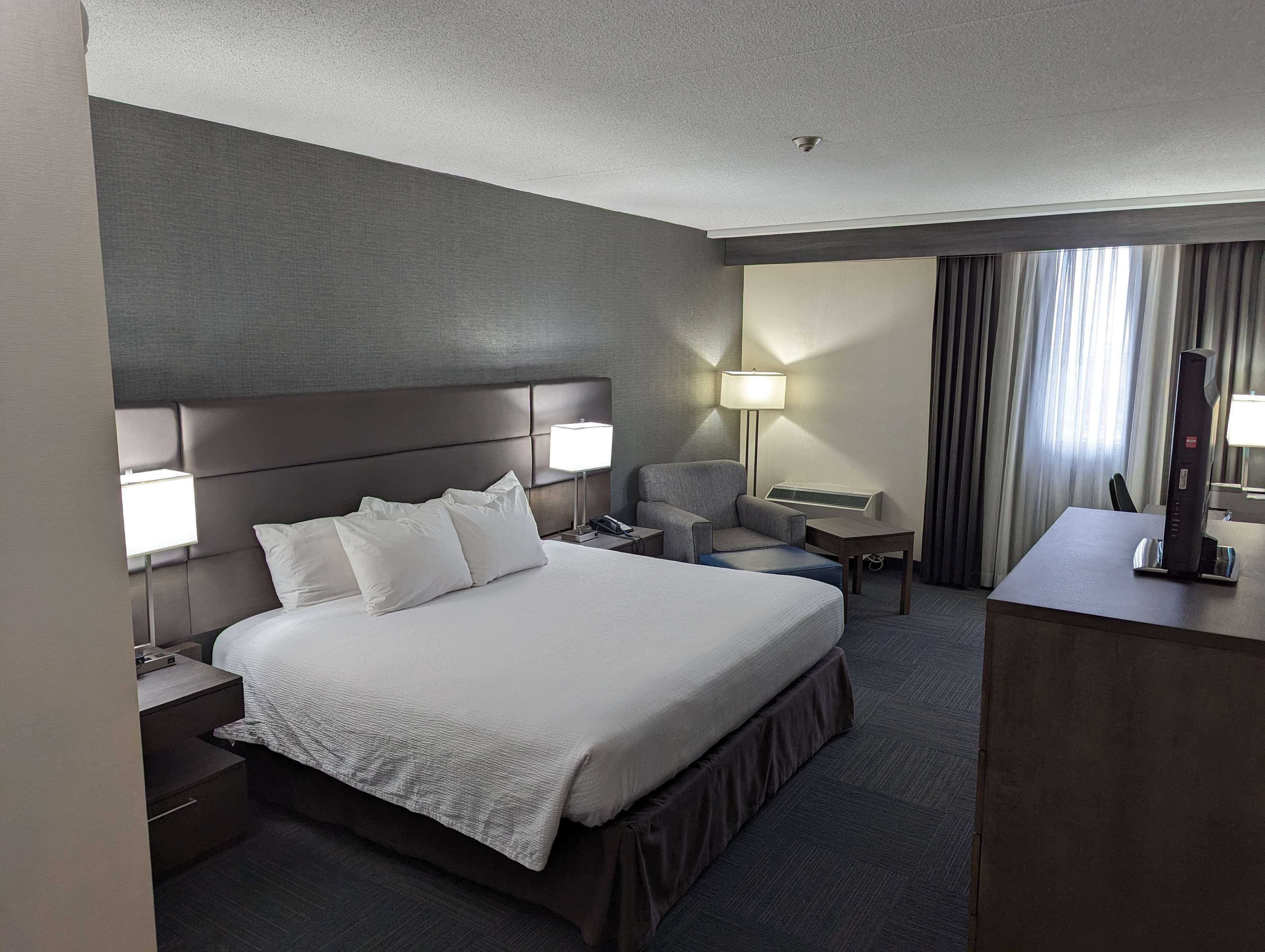 A hotel room with a large bed, a desk, a chair, and a lamp.