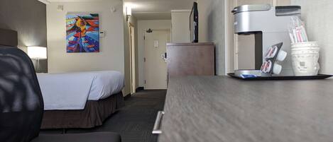 A hotel room with two beds, a desk with a coffee maker, a TV, and a painting on the wall.